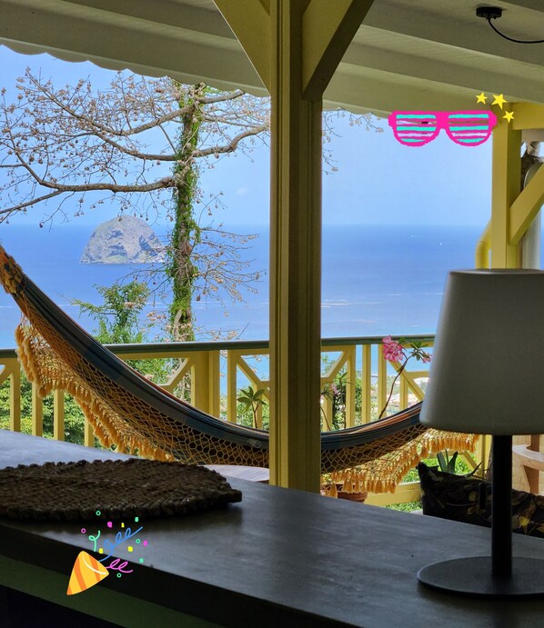 Una hamaca en un balcón con vista al mar y a una isla.