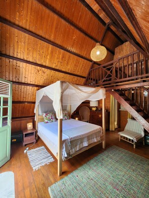 A rustic wooden room with a four-poster bed, a staircase, and a woven ceiling light fixture.