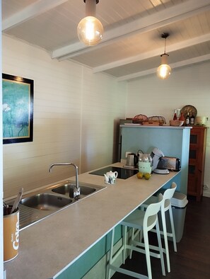 A kitchen with a sink, a countertop, a kettle, a toaster, and a fruit bowl.