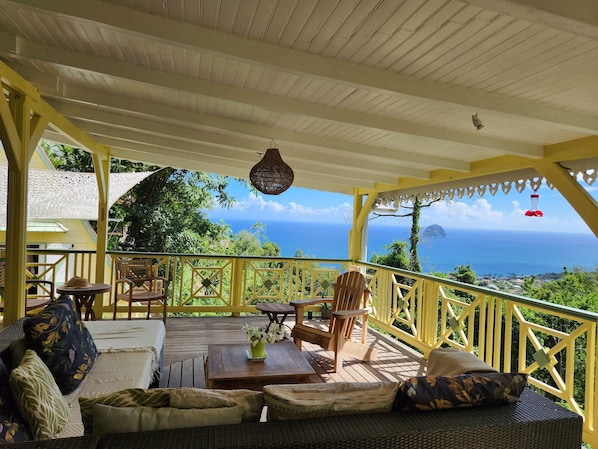 A covered outdoor seating area with a view of the ocean, wooden furniture, and a hanging light fixture. - Villa, lodge 6-7 pers, exceptional view, comfort and nature from the center. (Le Diamant)