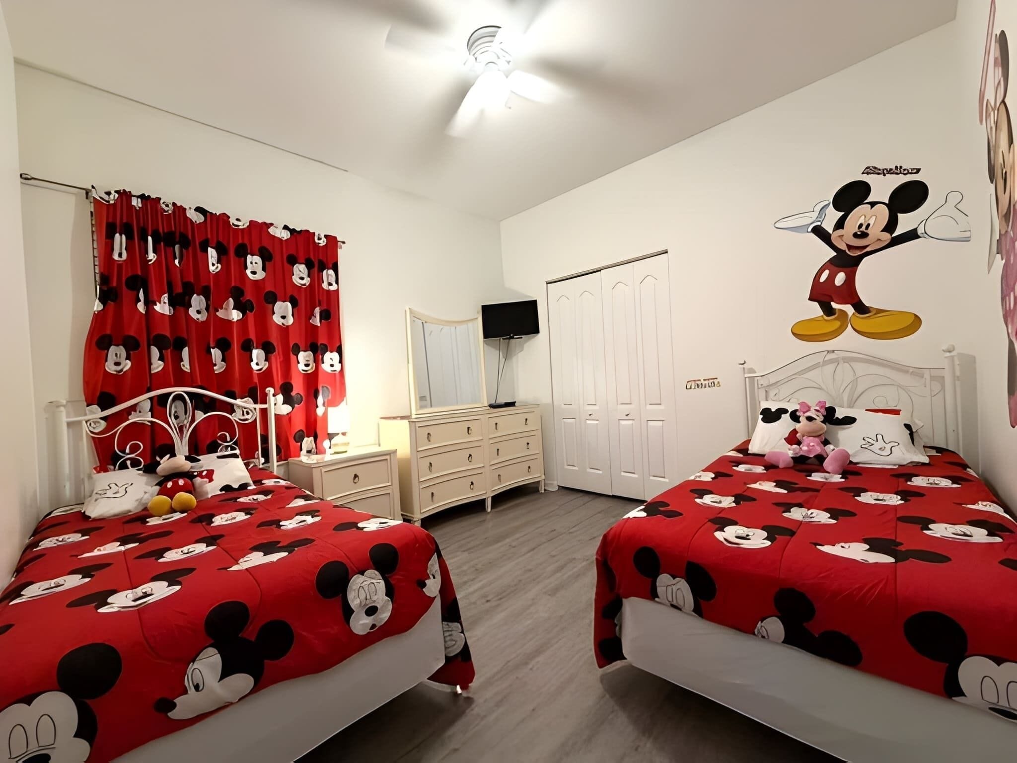 Ein Zimmer mit zwei Betten, einem Fernseher, einem Kleiderschrank und einer Wanddekoration mit Mickey Mouse.