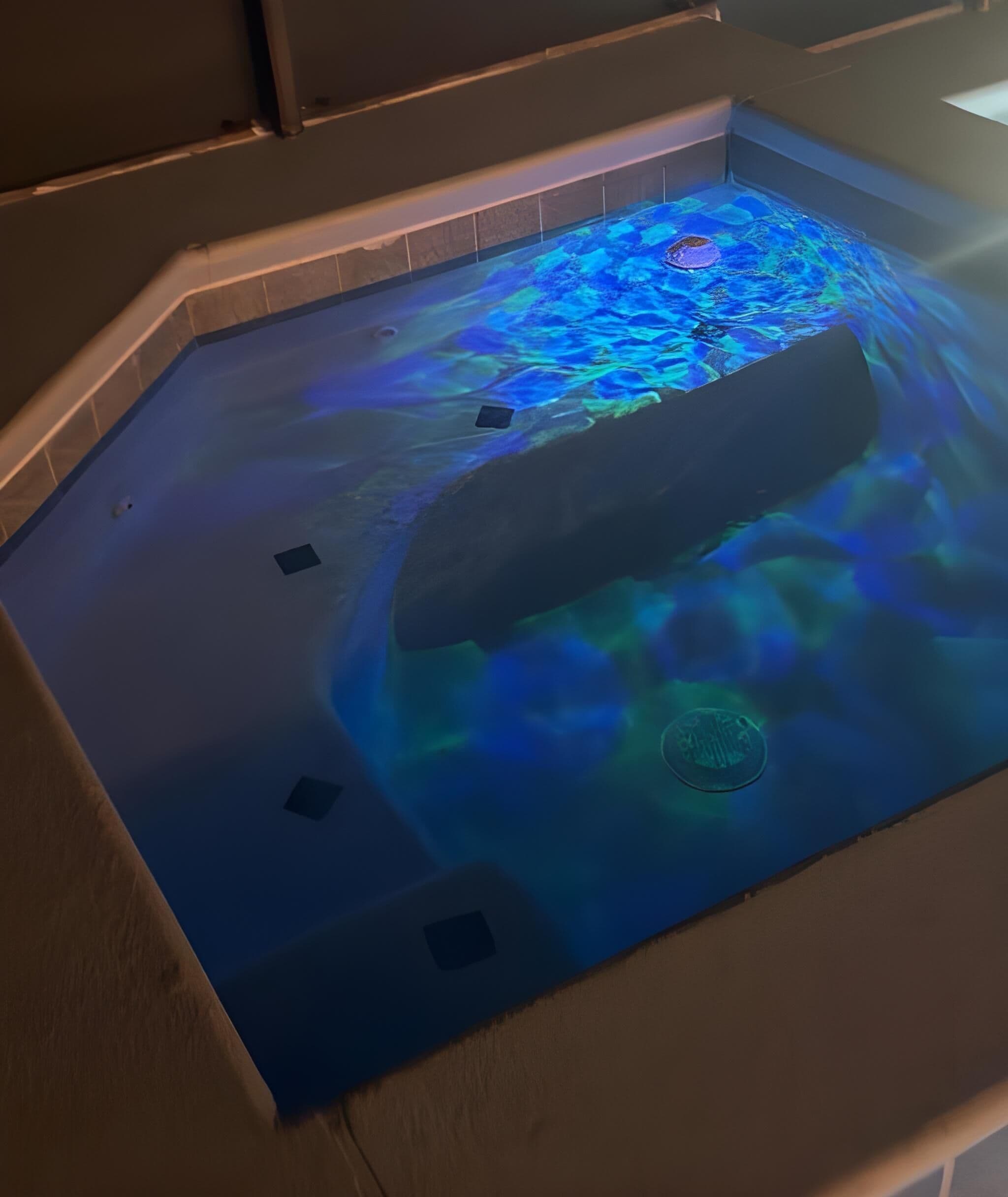 Een bubbelbad met blauw licht, omringd door betegelde vloer.
