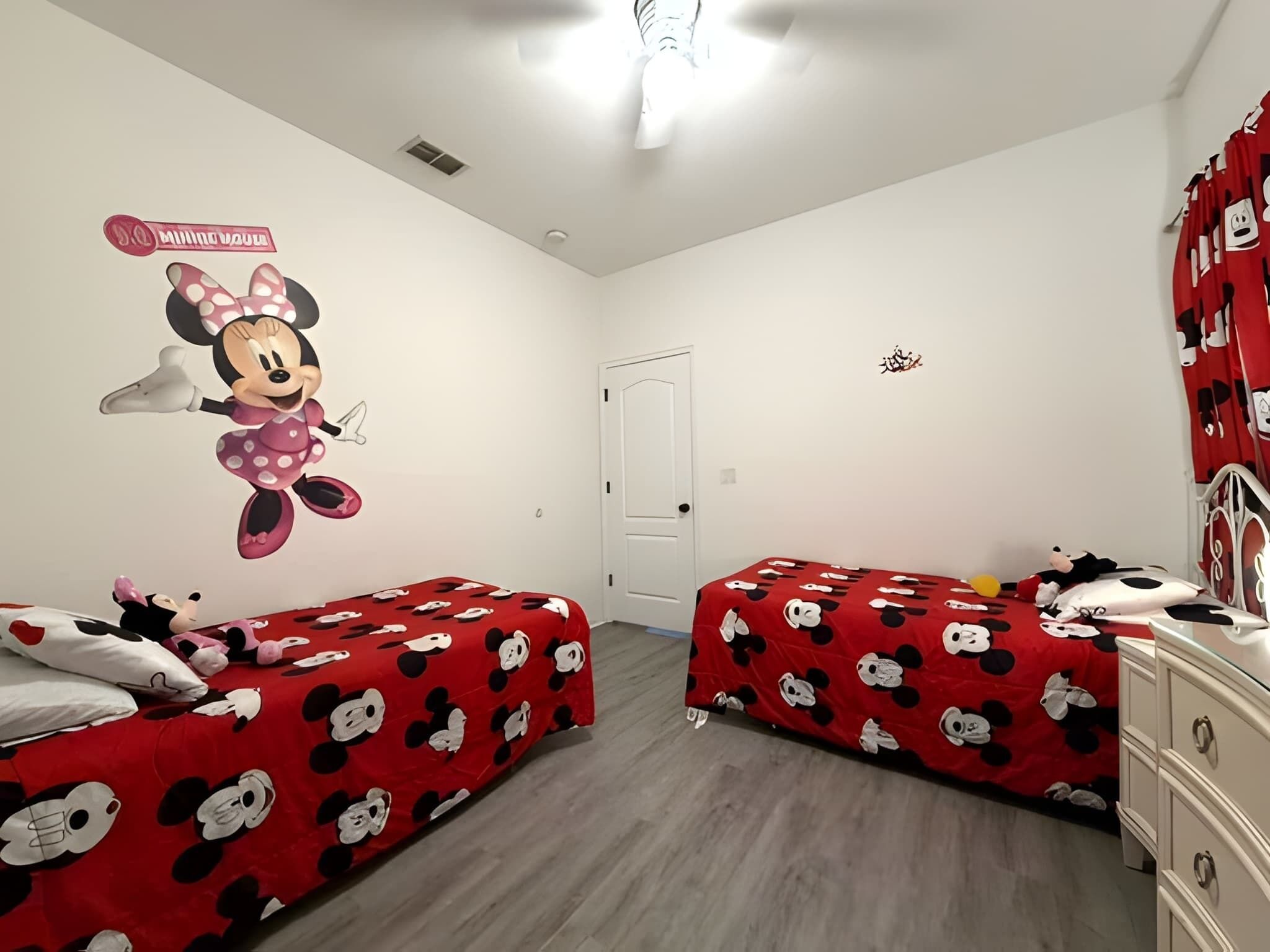 Ein Zimmer mit zwei Betten, jeweils mit Bettwäsche im Minnie-Maus-Design, einer Wandmalerei von Minnie-Maus und einer weißen Tür.