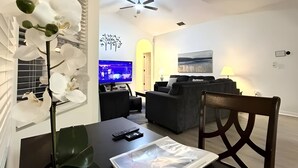 Un salón moderno con una mesa de comedor negra, una orquídea blanca y un ventilador de techo.