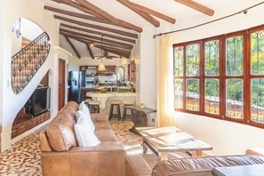 Ein geräumiges Wohnzimmer mit braunem Ledersofa, einem Couchtisch und einer Küchenzeile mit Esstisch und Barhocker.