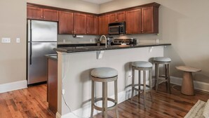 A modern kitchen with wooden cabinets, stainless steel appliances, a central island with stools, and a small round table.