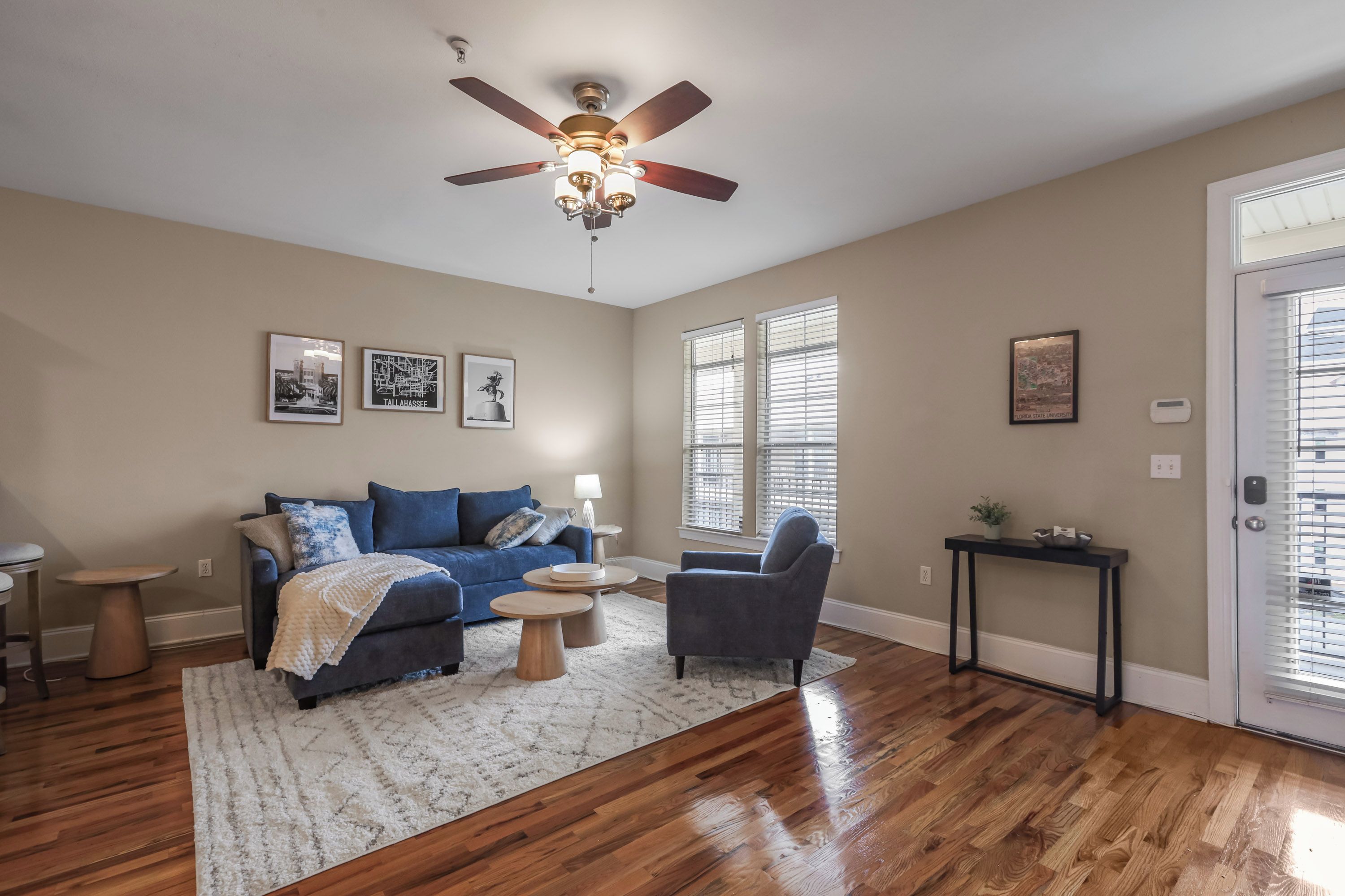 A living room with a blue sofa, a grey armchair, a ceiling fan, and hardwood flooring.