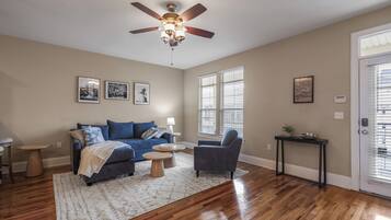A living room with a blue sofa, a grey armchair, a ceiling fan, and hardwood flooring.