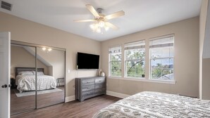 A bedroom with a bed, a dresser, a mirror, a ceiling fan, and a window with blinds.