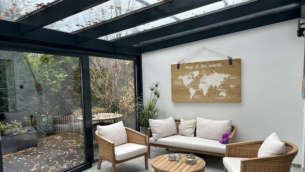 Une pièce moderne et bien éclairée, dotée d’un plafond en verre, d’un ensemble de canapés, d’une petite table ronde et d’une carte du monde accrochée au mur.