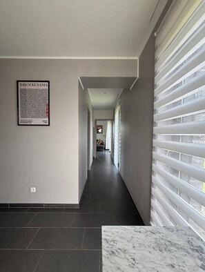A modern hallway with a dark tiled floor, a framed artwork on the left, and a window with blinds on the right. - Enjoyable 3-bedroom house with Saun in Belgian Ardenne for your getaway (Fauvillers)