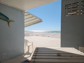 A beach view from a covered patio with a bench, a plastic chair, and a decorative fish. - Step out the door with toes in the sand and a drink in your hand! (Indian Shores)