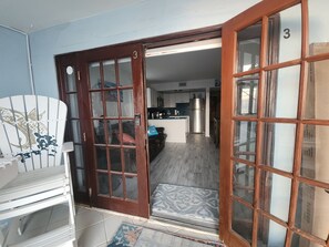 A room with a wooden door, a white chair with a fish design, and a kitchen area with a refrigerator and cabinets. - Step out the door with toes in the sand and a drink in your hand! (Indian Shores)