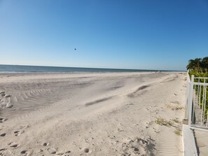 Una playa arenosa con huellas y una valla blanca.