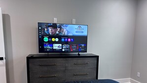 Een televisie op een zwarte dressoir met een streamingdienstinterface, diverse zenders en apps.