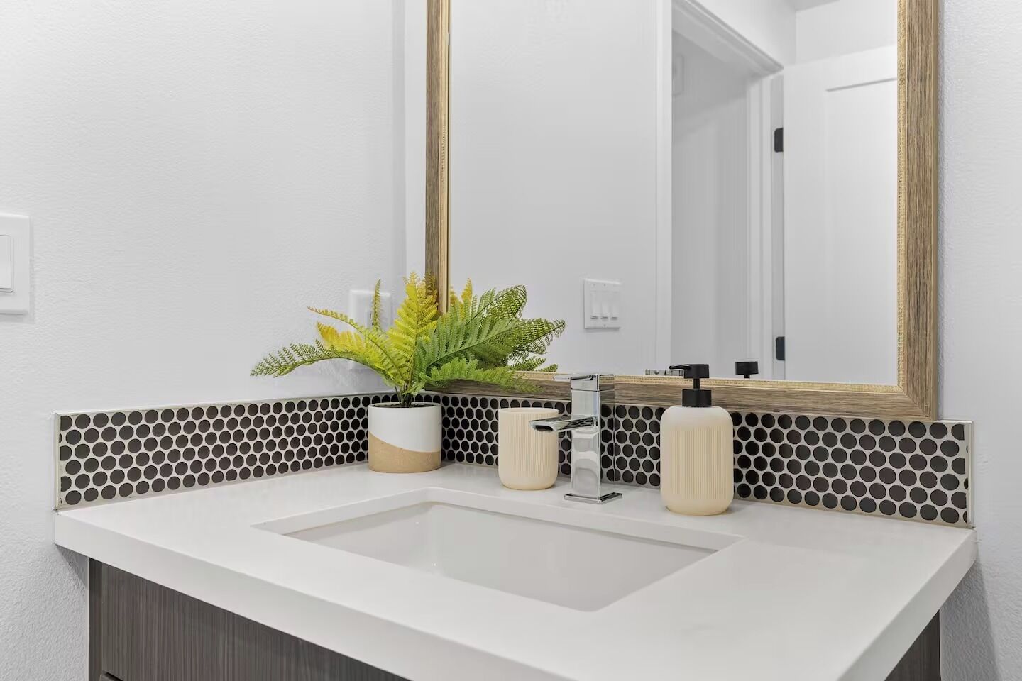 A bathroom with a white sink, two bottles of soap, a potted plant, and a large mirror with a wooden frame.