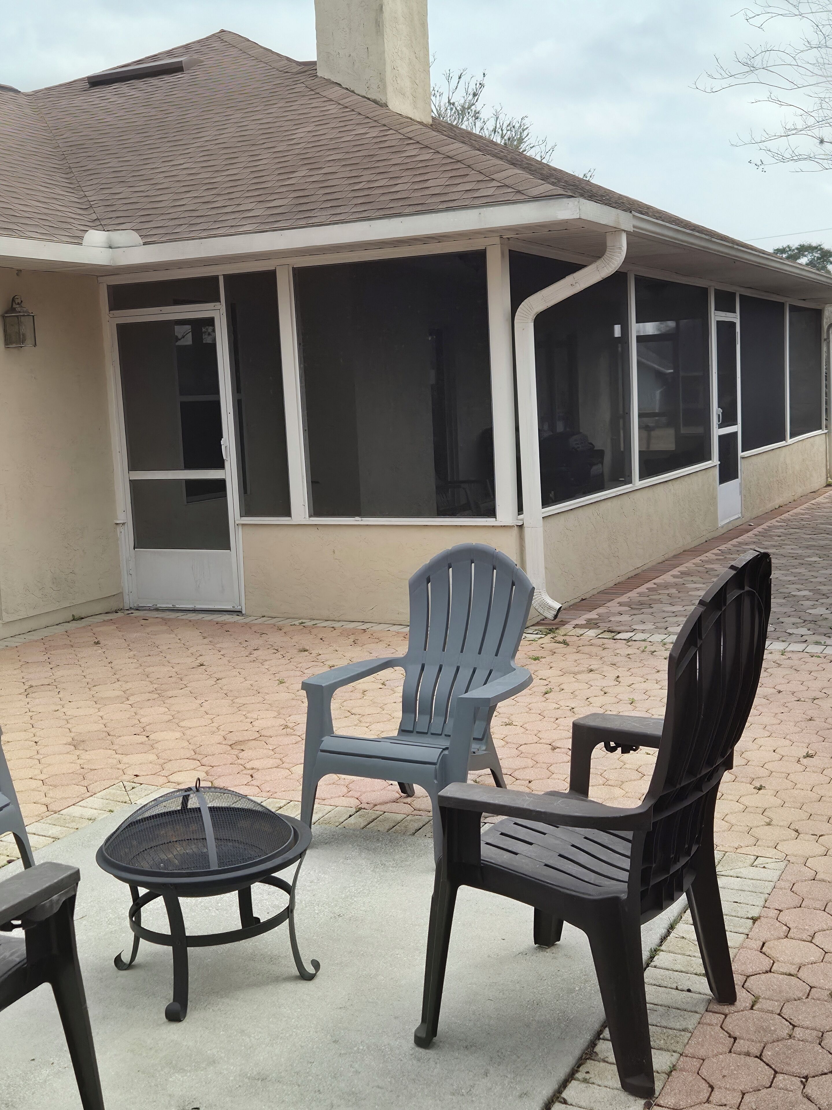A covered outdoor seating area with two chairs and a small table, a building with a sloped roof and large windows, and a paved walkway.