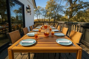 Eine Holzdielen-Terrasse mit einem langen Esstisch, umgeben von Stühlen und einer Glasreling.