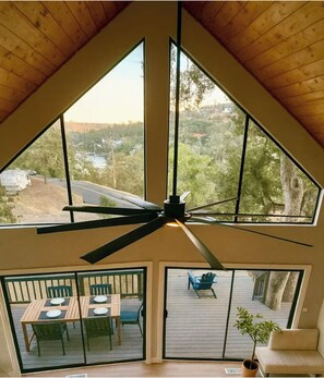 Ein Zimmer mit schrägen Wänden, großen Fenstern und einem Deckenventilator.