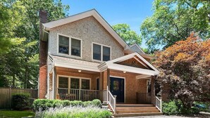 Une maison à deux étages avec un porche à l’avant, une cheminée en briques et un jardin bien entretenu.