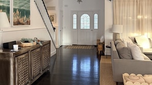Un vaste espace de vie doté d’un parquet en bois foncé, d’une porte blanche agrémentée de fenêtres en arc de cercle, d’un escalier et d’un grand tableau accroché au mur.
