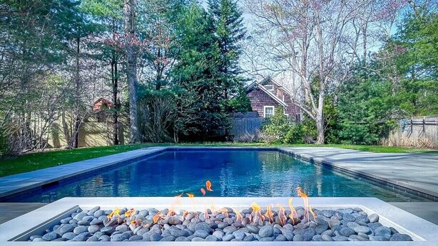 Une piscine rectangulaire bordée de galets, avec un foyer au centre.