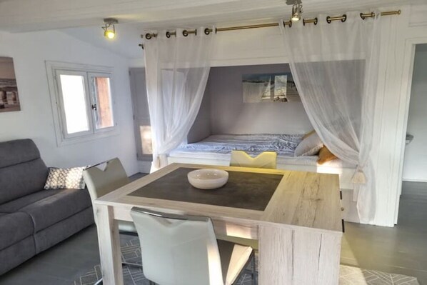 Een slaapkamer met een hemelbed, nachtkastje, stoel en raam.