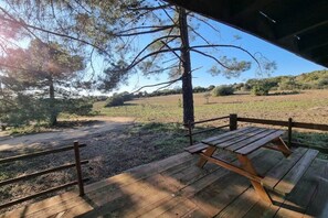 Een houten terras met een picknicktafel, omringd door een hek en bomen, met uitzicht op een veld.