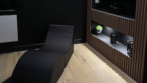 Habitació moderna amb una cadira de pell negra, un televisor penjat i un mur revestit de panells de fusta.