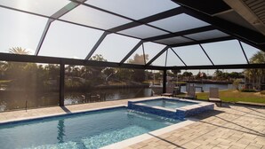 Piscina com estrutura de vidro, vista para um corpo d'água e área de estar externa.
