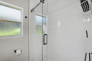 Ein modernes Badezimmer mit Duschkabine aus Glas, Toilettenpapierhalter und Fenster mit Blick auf Grünflächen.