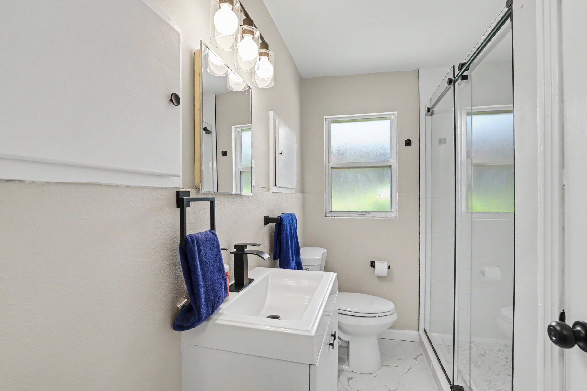 A bathroom with a white sink, a toilet, a shower with glass doors, and a window.