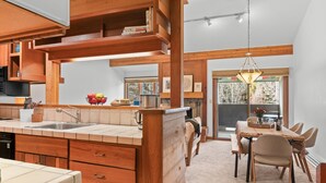 A modern kitchen with wooden cabinetry, a large island with a sink, and a dining area with a table and chairs. - RMR: Alpine Fir 722 Condo in The Aspens/Wilson, WY (Wilson)