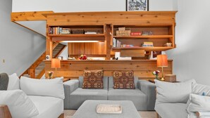 A modern living room with a grey sofa set, a wooden bookshelf, and a staircase leading to an upper level. - RMR: Alpine Fir 722 Condo in The Aspens/Wilson, WY (Wilson)