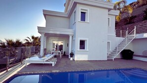 Ein modernes Haus mit Schwimmbecken, einer überdachten Terrasse und einer Treppe, die zu einer oberen Ebene führt.