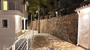 A stone-paved pathway leading to a white building with a balcony, surrounded by a stone wall and palm trees. - Inviting villa above Denia with views of the mountains and sea. Pets ❤️ (Pedreguer)
