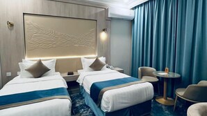 A hotel room with two beds, a small round table, a chair, and a large window with curtains. - The High View (Al Baha)