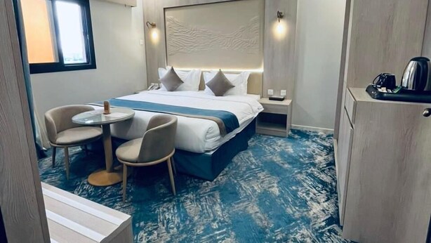A hotel room with a bed, a desk, a chair, a small table, and a window. - The High View (Al Baha)