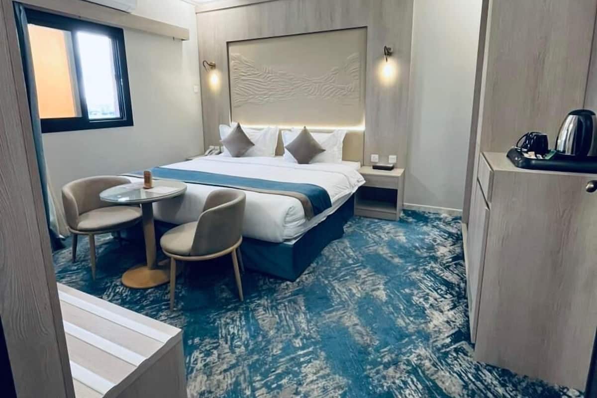 A hotel room with a bed, a desk, a chair, a small table, and a window.