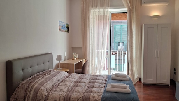 Une chambre à coucher comprenant un lit, un bureau, une chaise, une armoire et donnant sur l’extérieur.