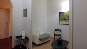 Un salon avec un canapé, une petite table, un fauteuil et un tableau accroché au mur.