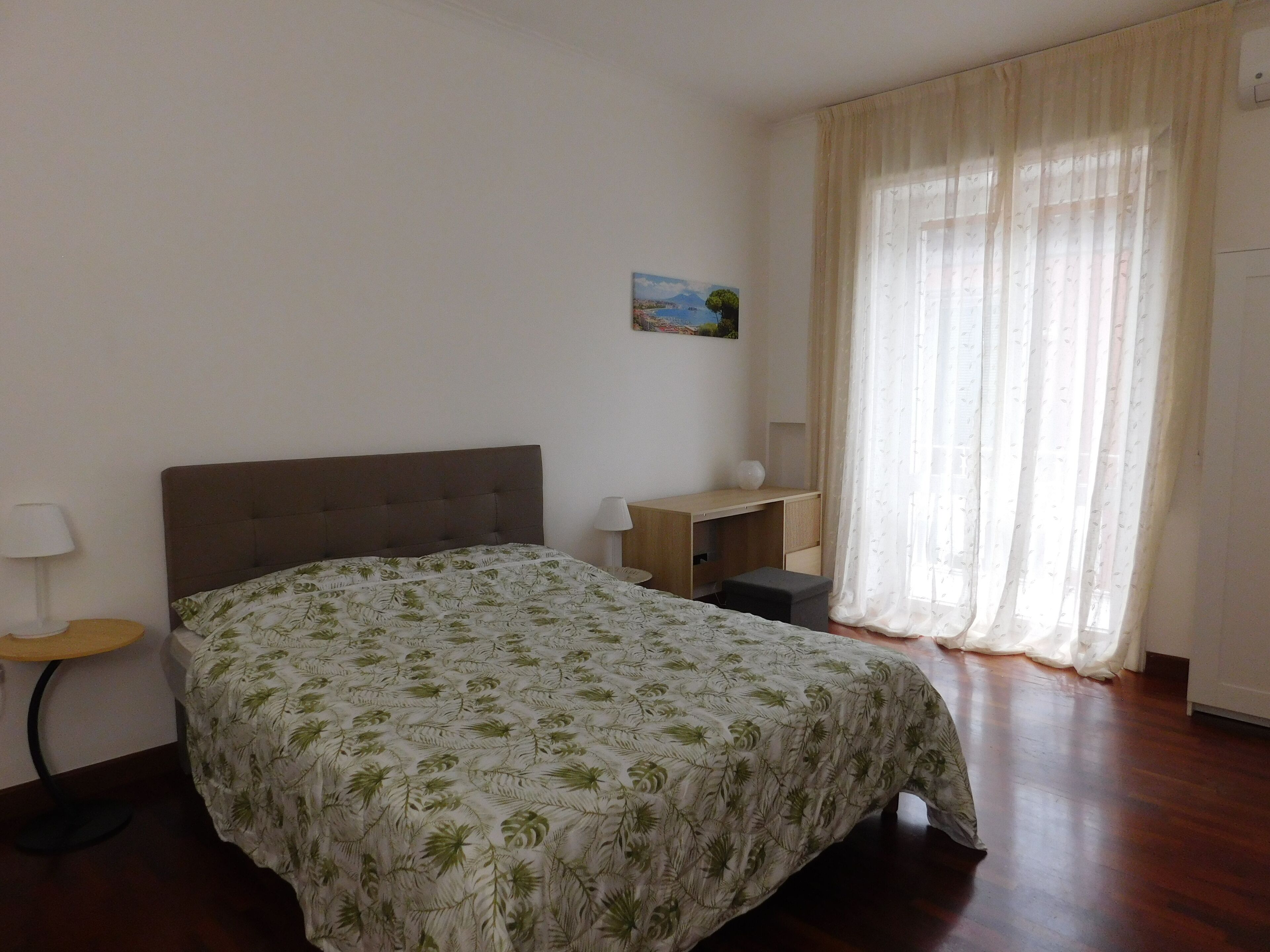 A bedroom with a bed, a desk, a chair, a lamp, and a window with curtains.