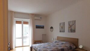 Une chambre à coucher avec un lit, des tables de chevet, une fenêtre avec des rideaux et des œuvres d’art murales.