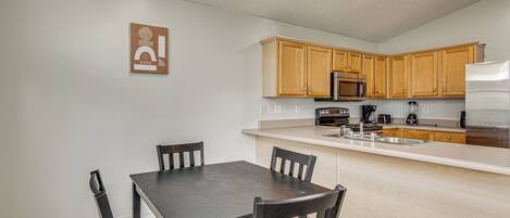 A kitchen with wooden cabinets, a black countertop, and a stainless steel refrigerator.