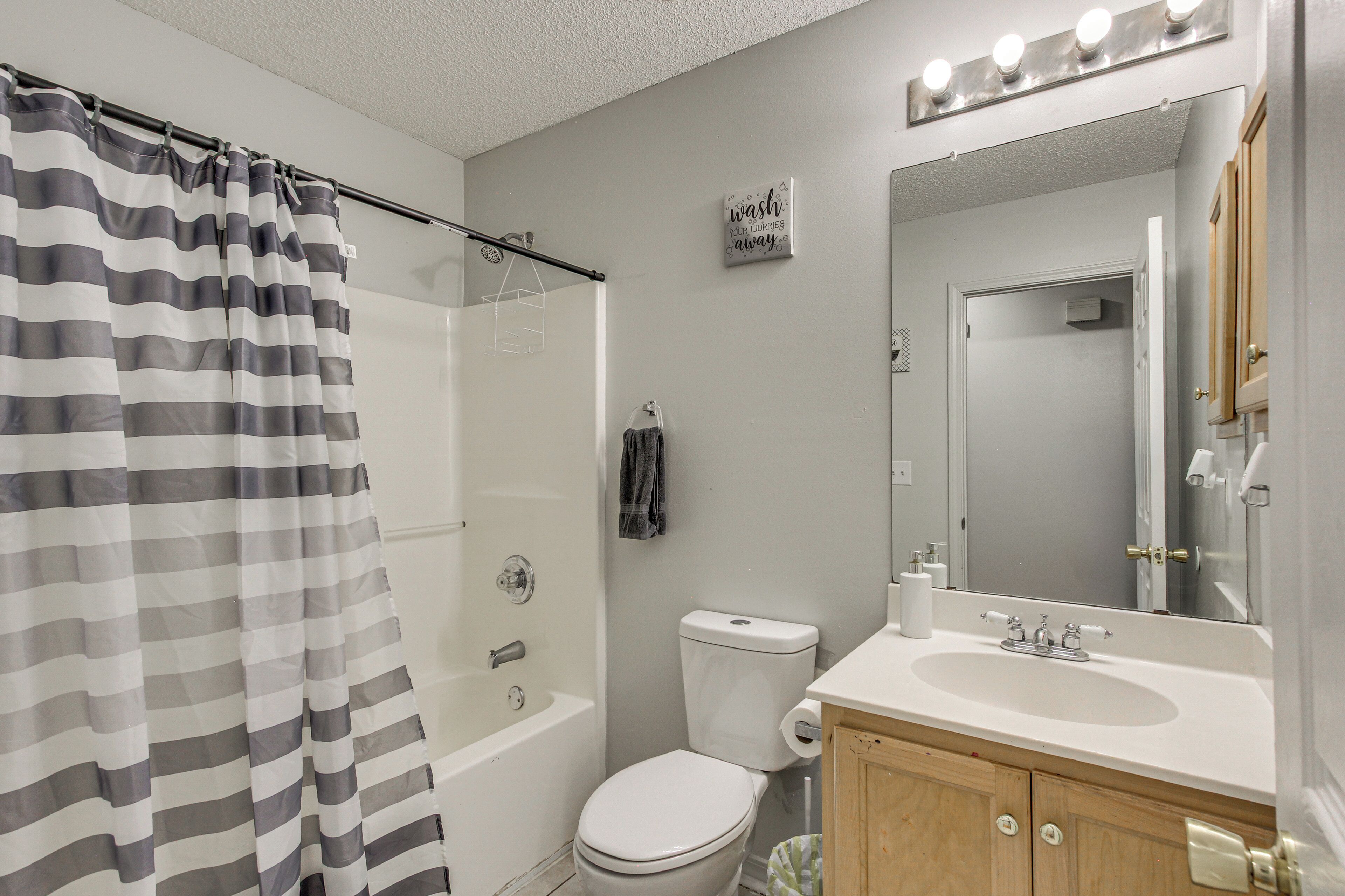A bathroom with a shower curtain, toilet, sink, and mirror.