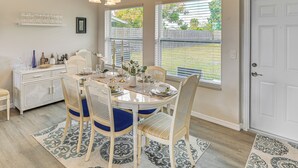 Un coin repas avec une table blanche dressée pour quatre personnes, entourée de chaises en osier avec des coussins bleus.