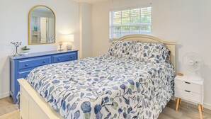 Une chambre à coucher comprenant un lit, une commode avec des tiroirs, une table de chevet avec une lampe, une fenêtre avec des stores et un miroir fixé au mur.