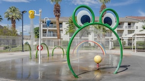 A water play area with circular and arch-shaped structures, a yellow ball, and a building with balconies in the background. - Resort Perks & Family Fun! St George Retreat (St. George)