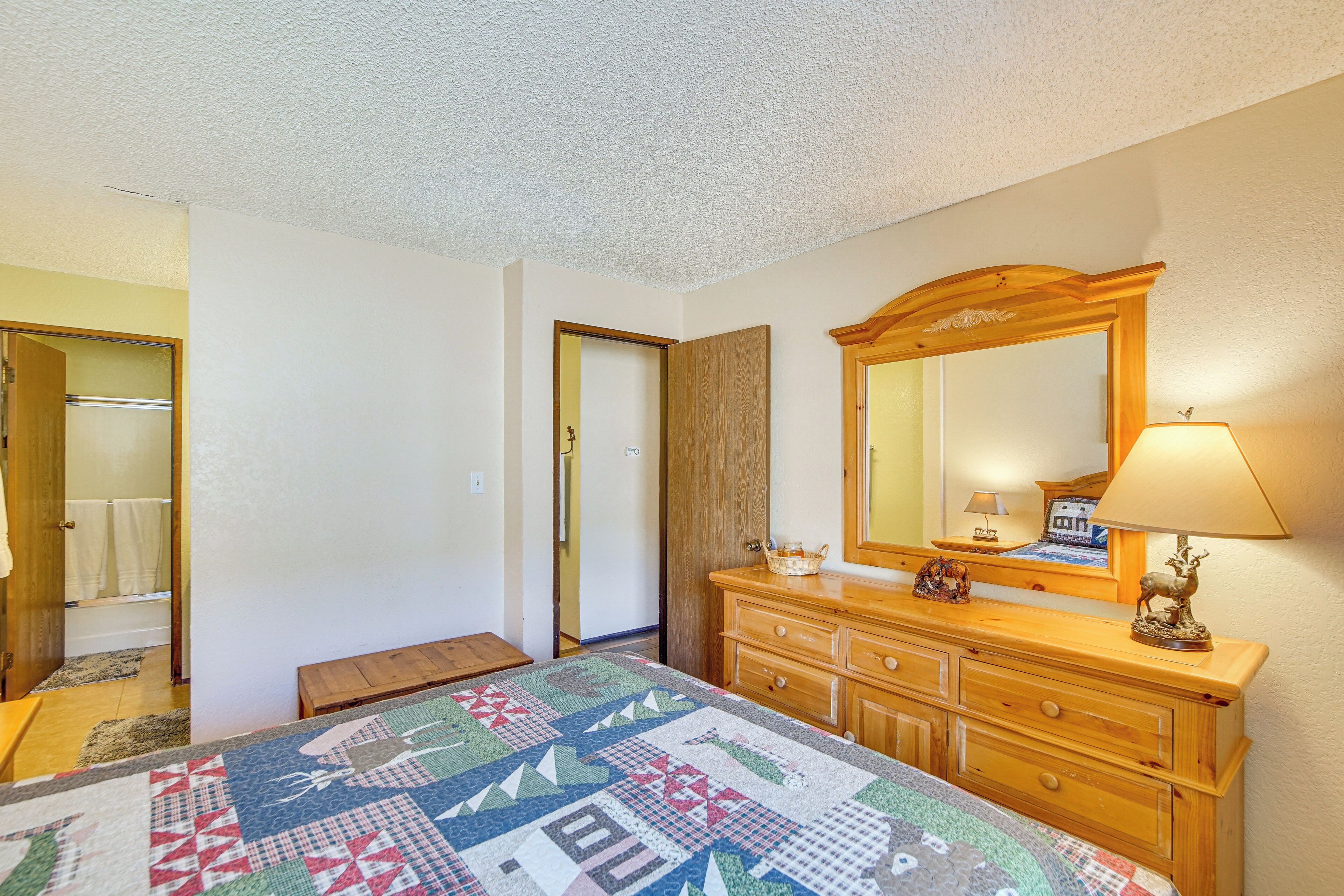 A bedroom with a wooden dresser, a mirror, a quilt, and a bench.