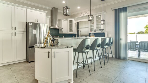 Una cocina moderna con armarios blancos, electrodomésticos de acero inoxidable y una barra con taburetes.